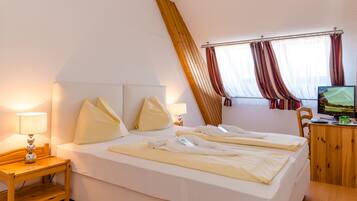 Een hotelkamer met een groot bed, een houten nachtkastje met een lamp, een bureau met een computer, en een raam met gordijnen.