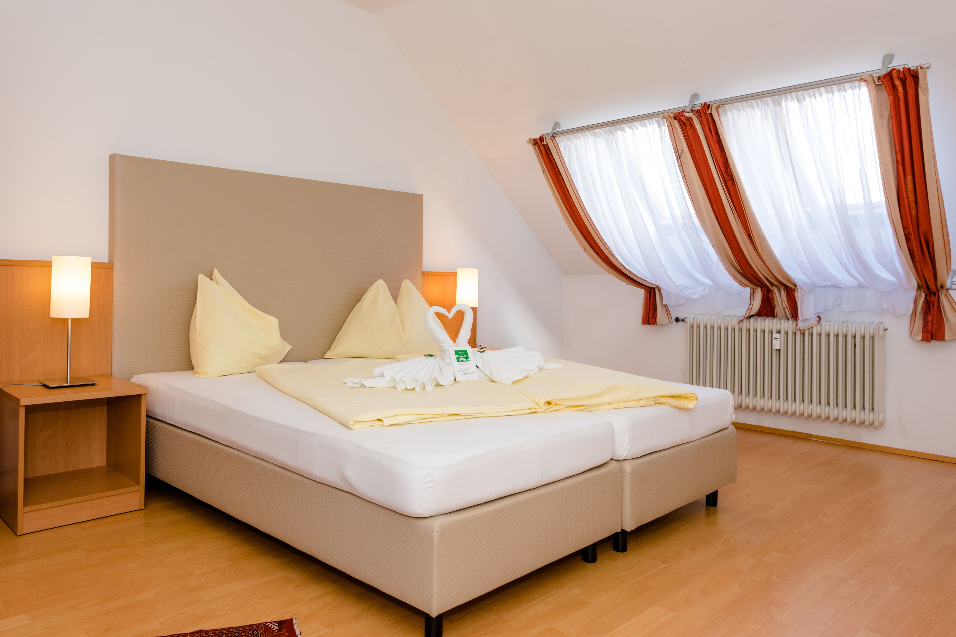 Una cama bien hecha con almohadas, una mesita de noche con lámpara y una ventana con cortinas.