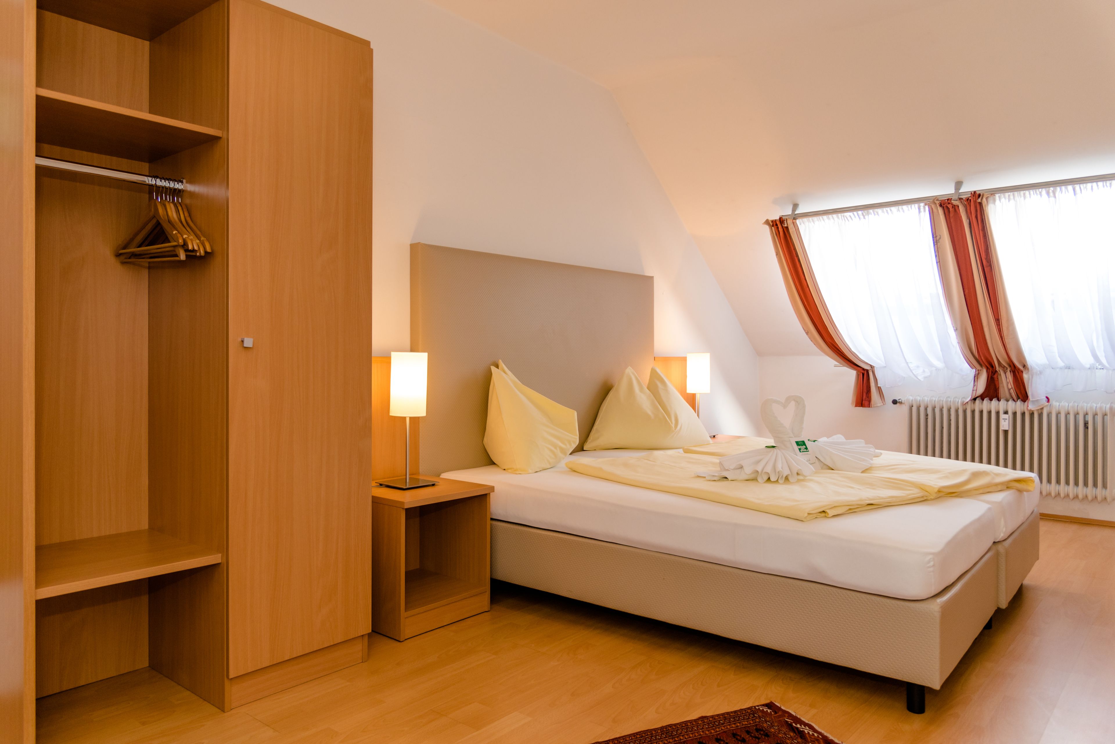 A bedroom with a bed, bedside lamps, a wooden wardrobe, and a radiator.