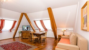 Un loft espacioso con techo alto, vigas de madera a la vista, un comedor con mesa y sillas, un sofá y una televisión.