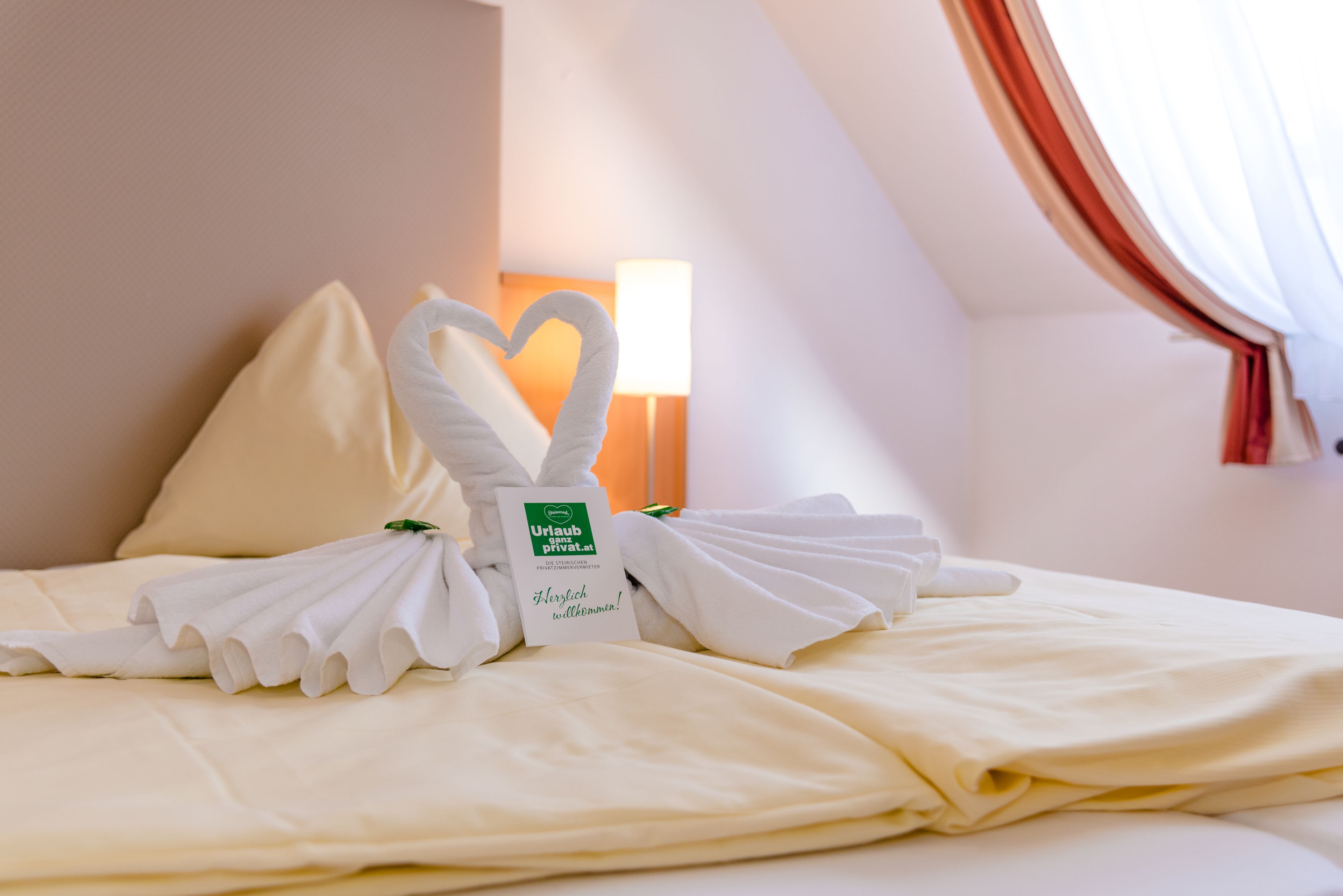 Un lit bien fait, agrémenté d’une serviette pliée en forme de cœur et d ’une pancarte indiquant si la chambre est disponible.