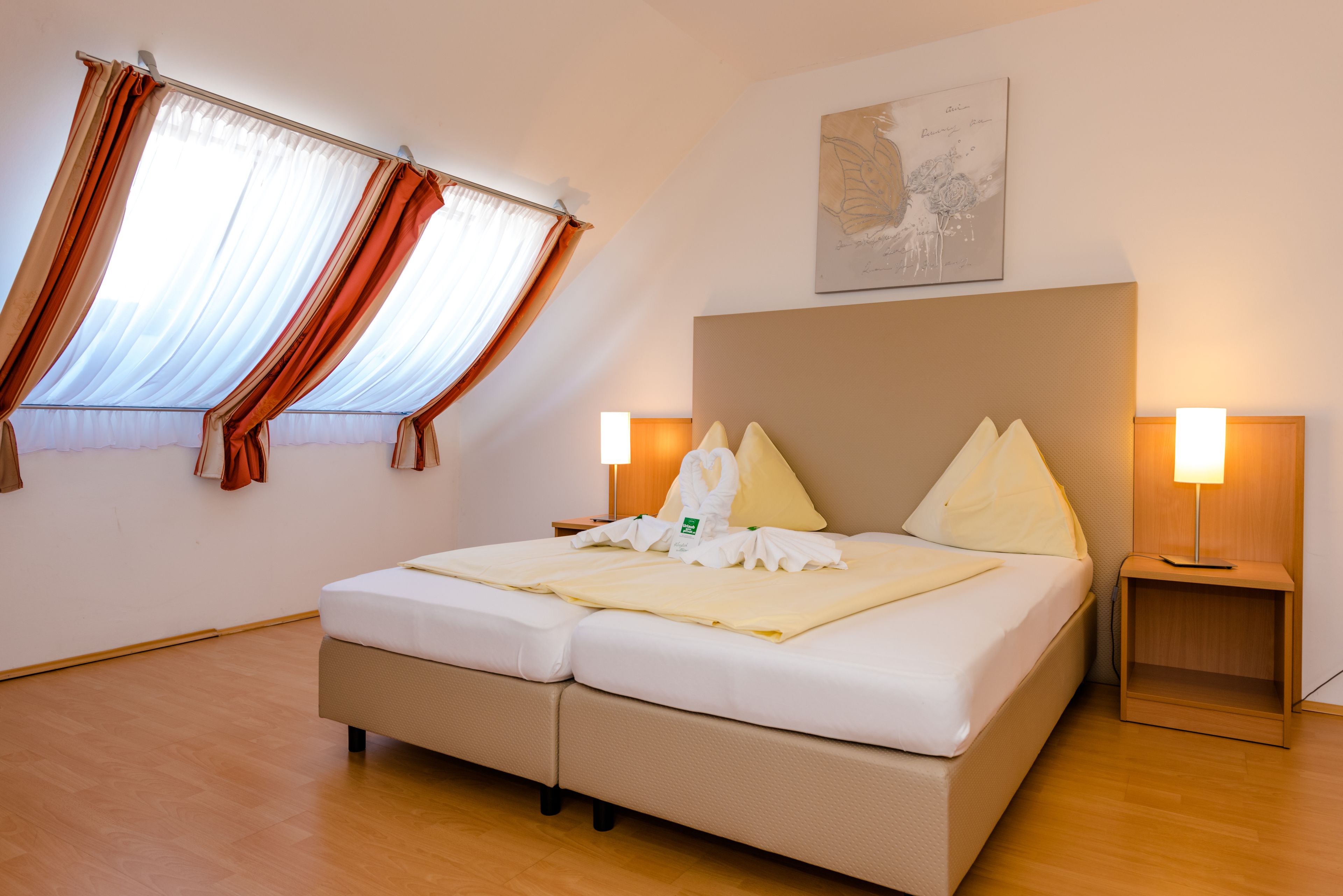 Een hotelkamer met een bed, twee bedlampen, een raam met gordijnen en een kunstwerk aan de muur.