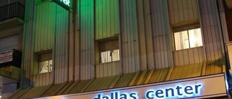 A hotel with a neon sign reading "HOTEL DALLAS CENTER" and a marquee sign below stating "HOTEL DALLAS CENTER".