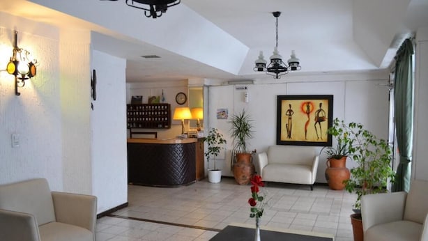 Un vestíbulo de hotel con un mostrador de recepción, dos sofás, una mesa de centro y plantas en macetas.