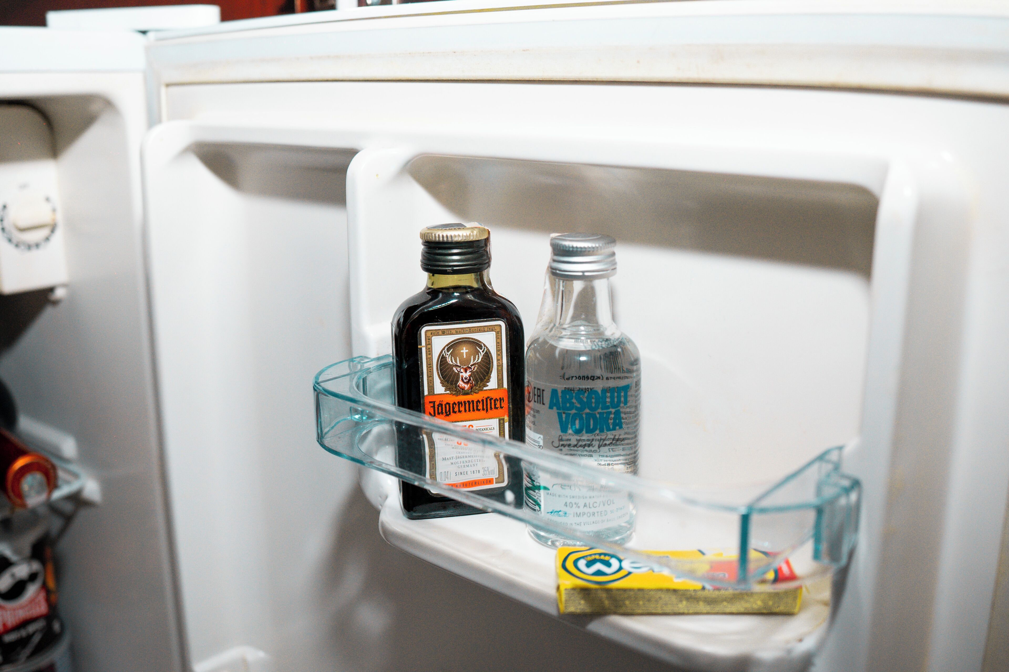 A refrigerator with a shelf containing a bottle of Jägermeister and a bottle of Absolut Vodka.