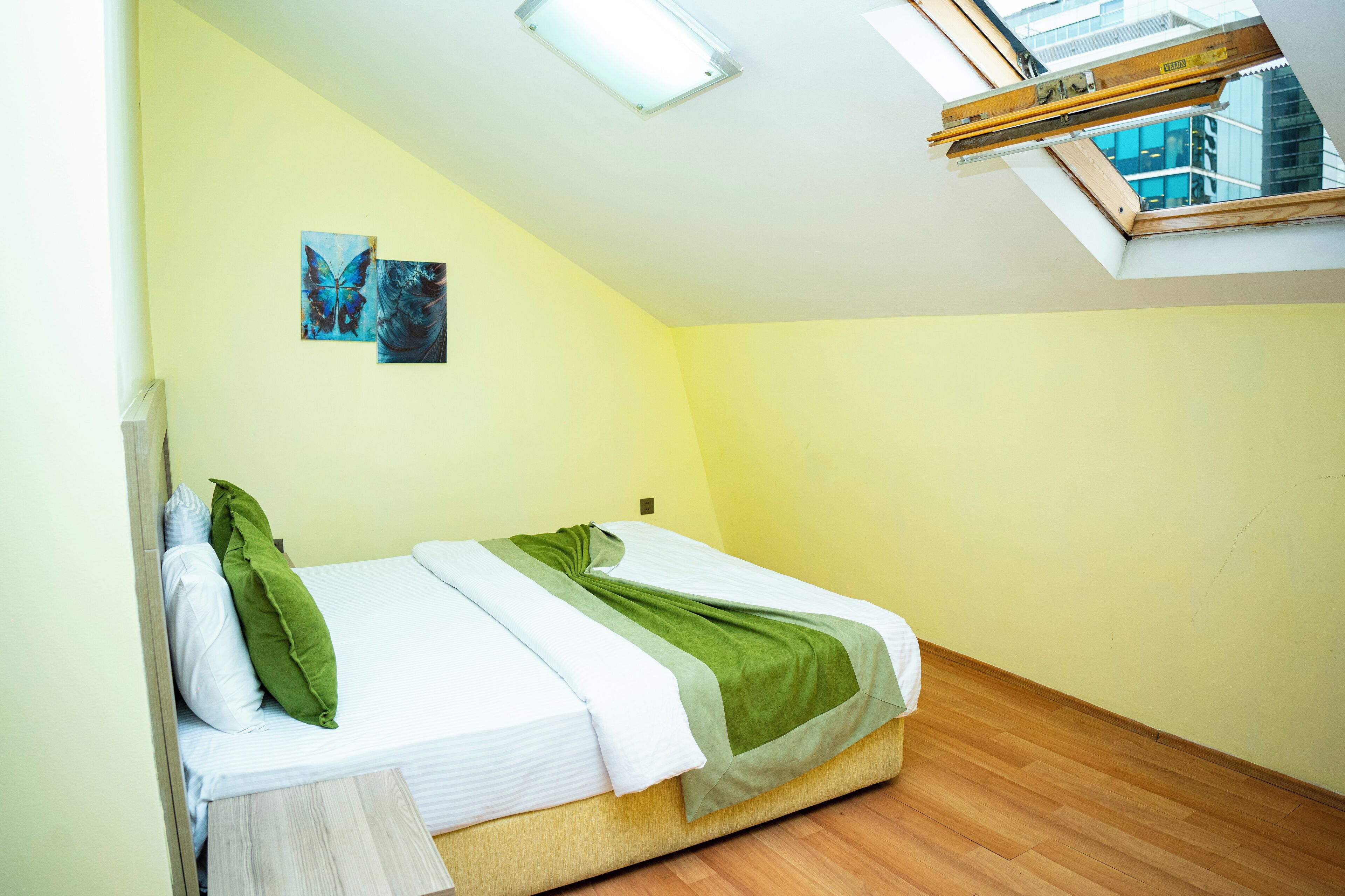 Un dormitorio con tragaluz, una cama con ropa de cama verde y blanca, y dos cuadros colgados en la pared.