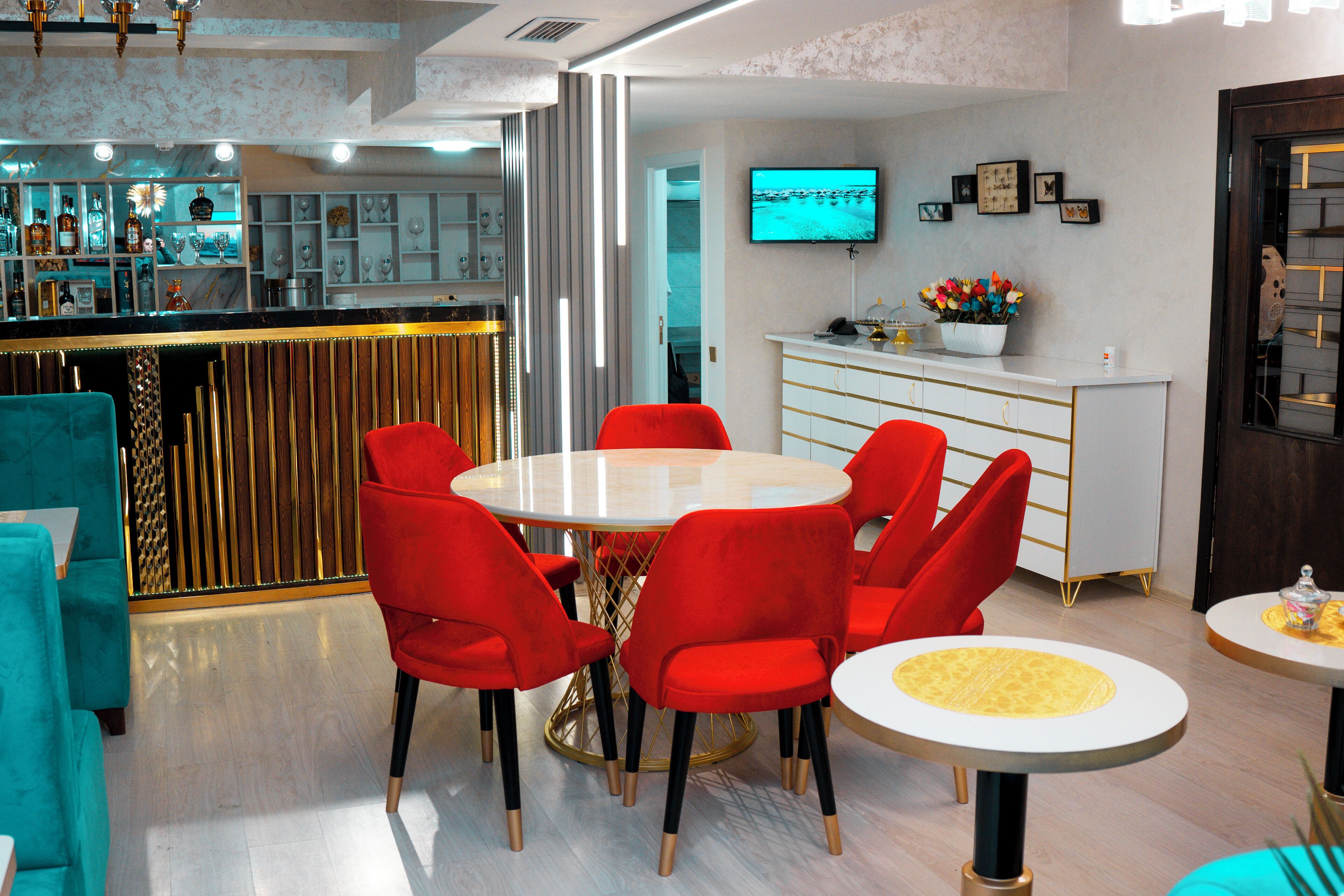 Een moderne hotellobby met een bar, een ronde eettafel met rode stoelen en een aan de muur bevestigde televisie.