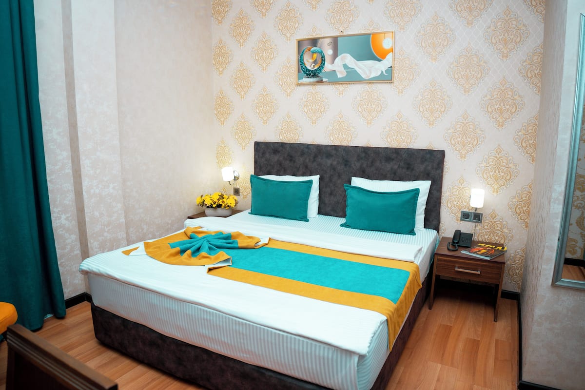 A neatly made bed with a striped bedspread, a bedside table with a lamp, and a wall with patterned wallpaper.