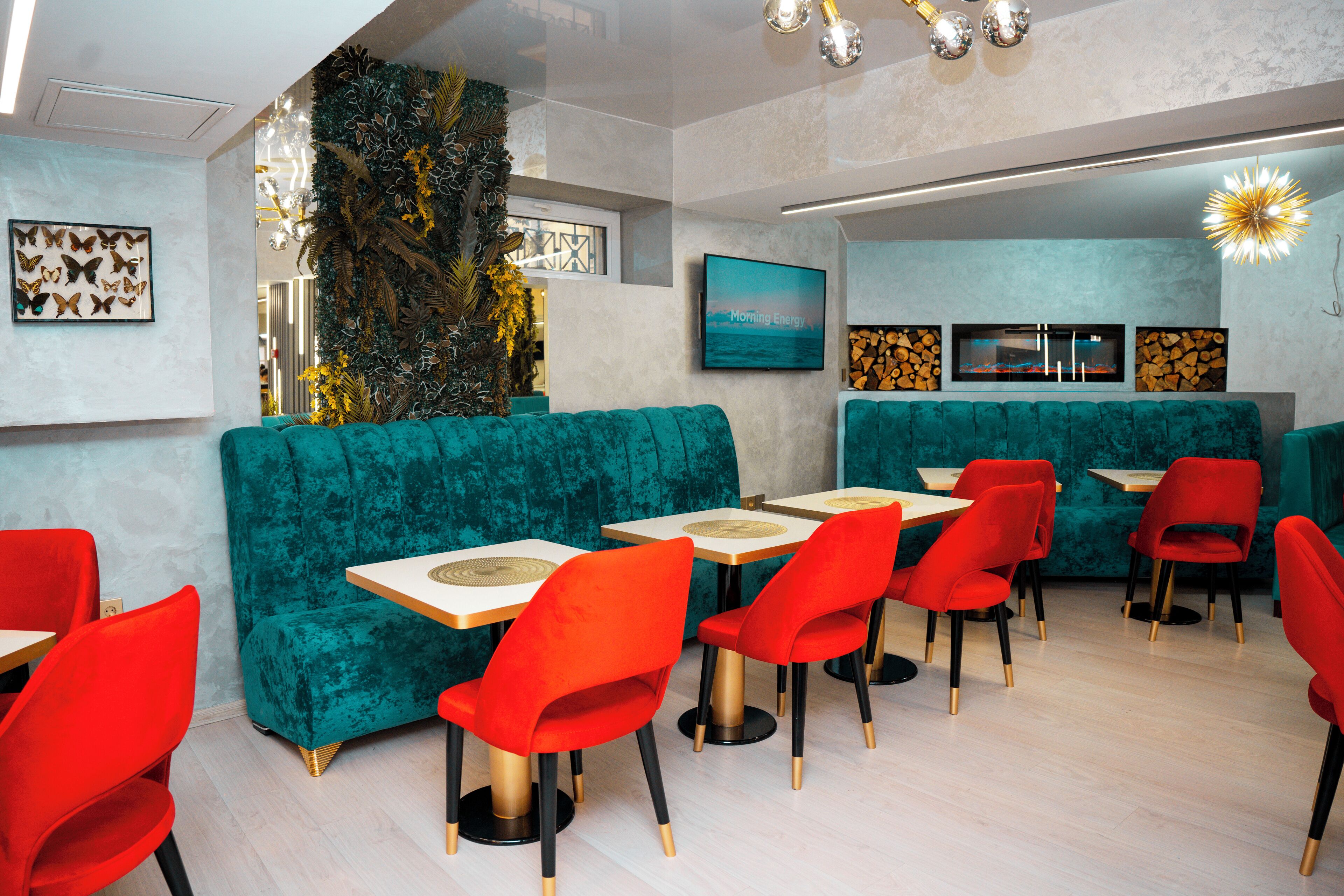 A modern restaurant with teal upholstered booths, red chairs, and a light wood floor.