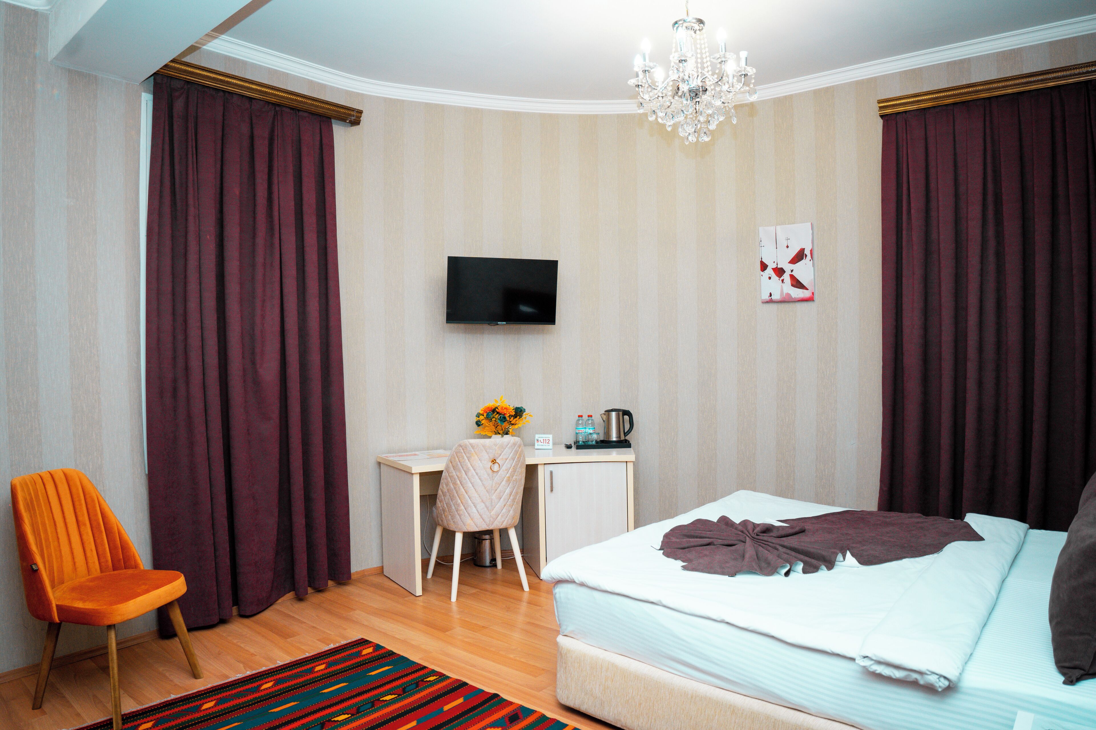 Ett hotellrum med en säng, ett skrivbord, en stol, en tv och en kristallkrona.