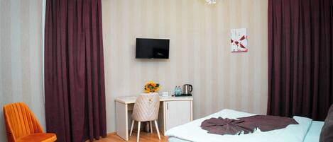 Ett hotellrum med en säng, ett skrivbord, en stol, en tv och en kristallkrona.