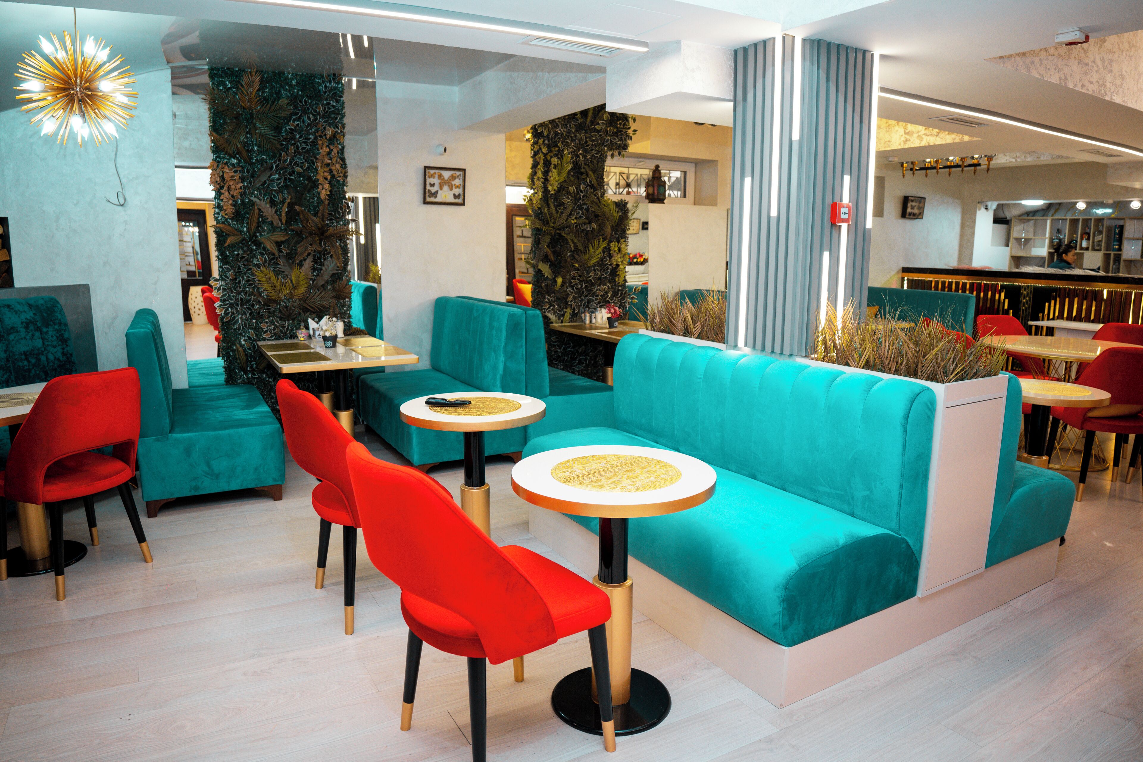 A modern restaurant with teal and red seating, wooden tables, and a decorative wall.