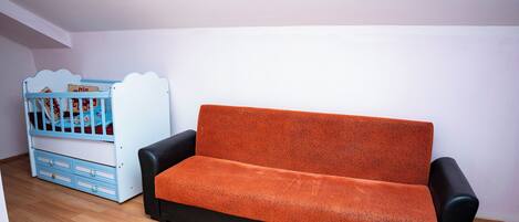 A room with a black and orange sofa, a blue crib, and wooden flooring.