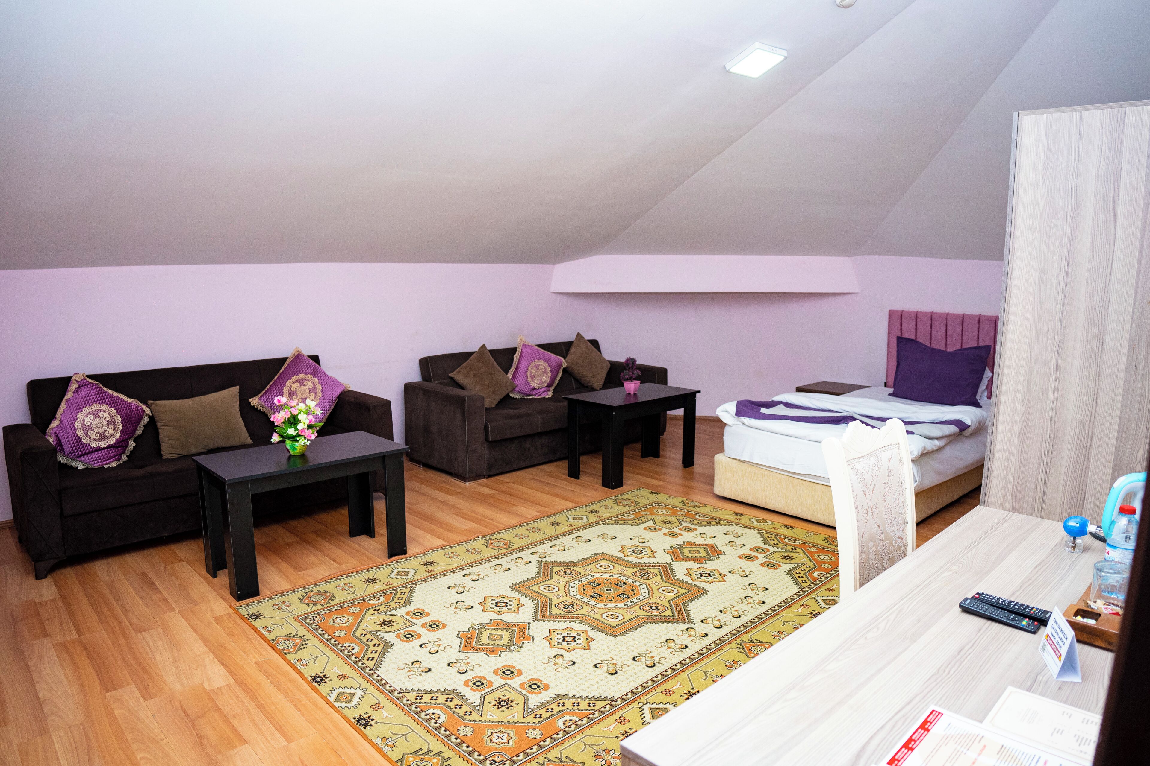 A cozy loft-style living space with a high ceiling, a sofa set, a dining table, and a bed.