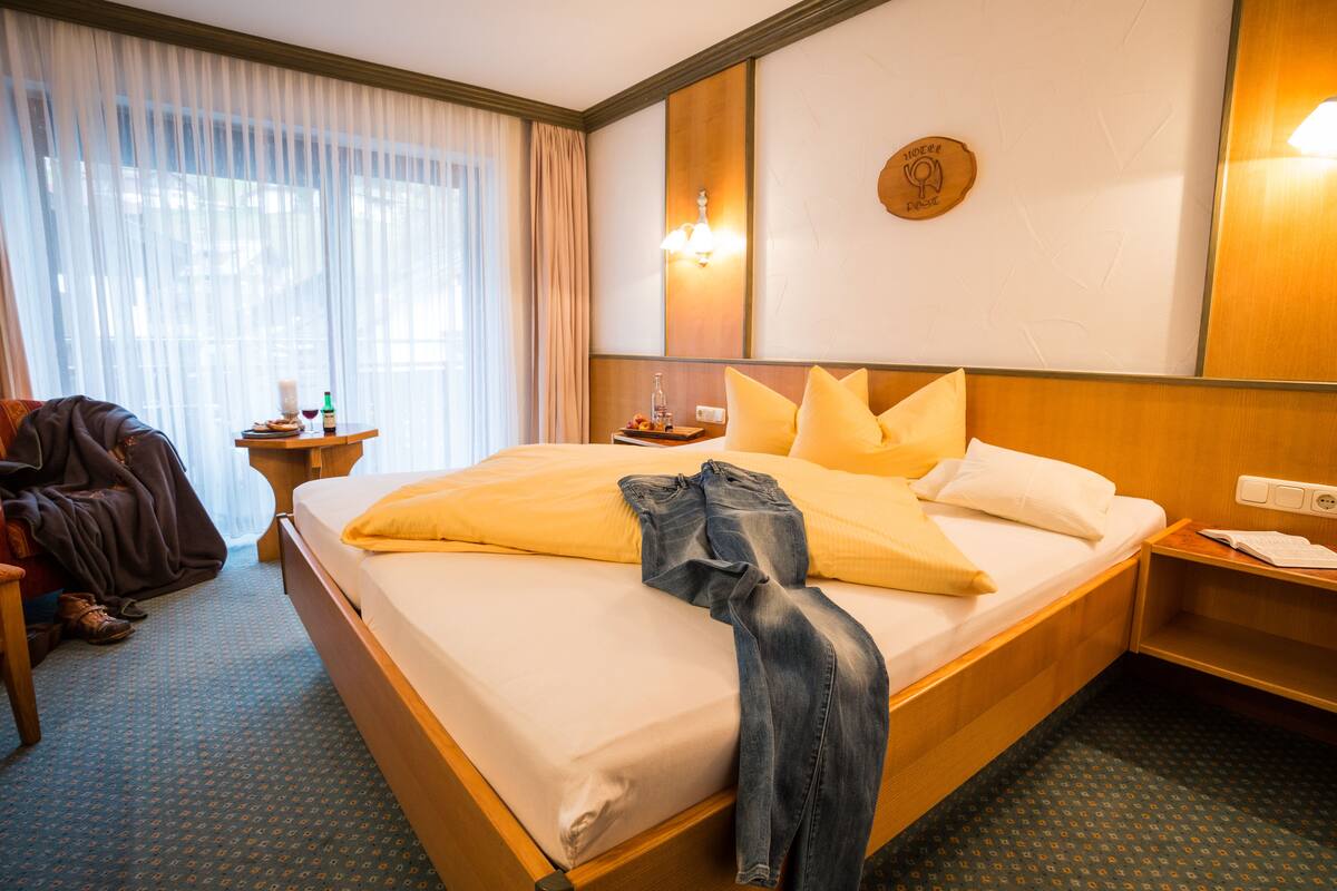 Quarto de hotel com uma cama grande, uma mesa de cabeceira e uma janela com cortinas.