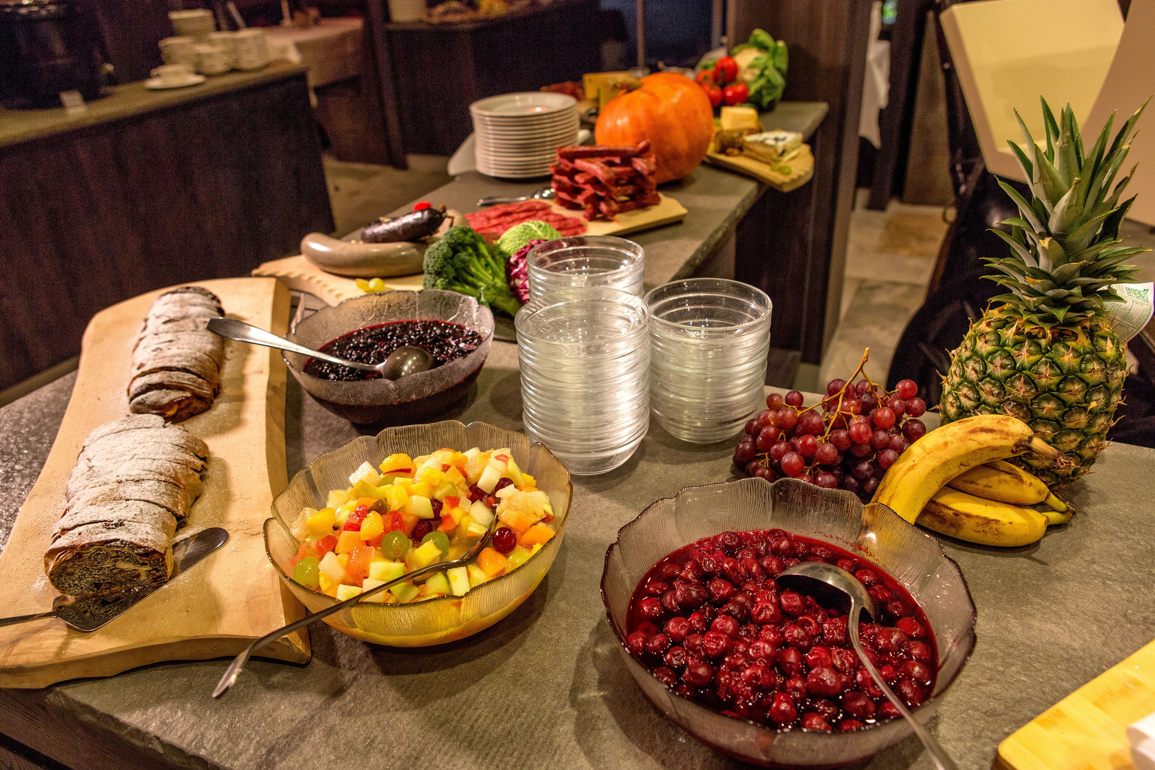Una mesa de buffet con diversas opciones de comida, incluyendo un pan rebanado, ensalada de frutas, salsa de arándanos y una piña.