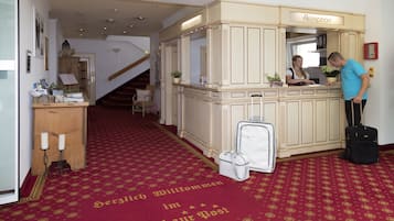 Una recepción con un letrero que dice "Rezeption" en el vestíbulo de un hotel, con alfombra roja y una escalera al fondo.