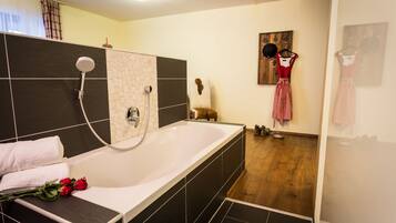 A modern bathroom with a large bathtub, a shower, and a wooden floor.