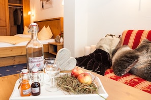 A cozy room with a wooden bed, a plush red sofa, and a table with a bottle, glasses, and apples. - Haller´s Post Hotel (Mittelberg)