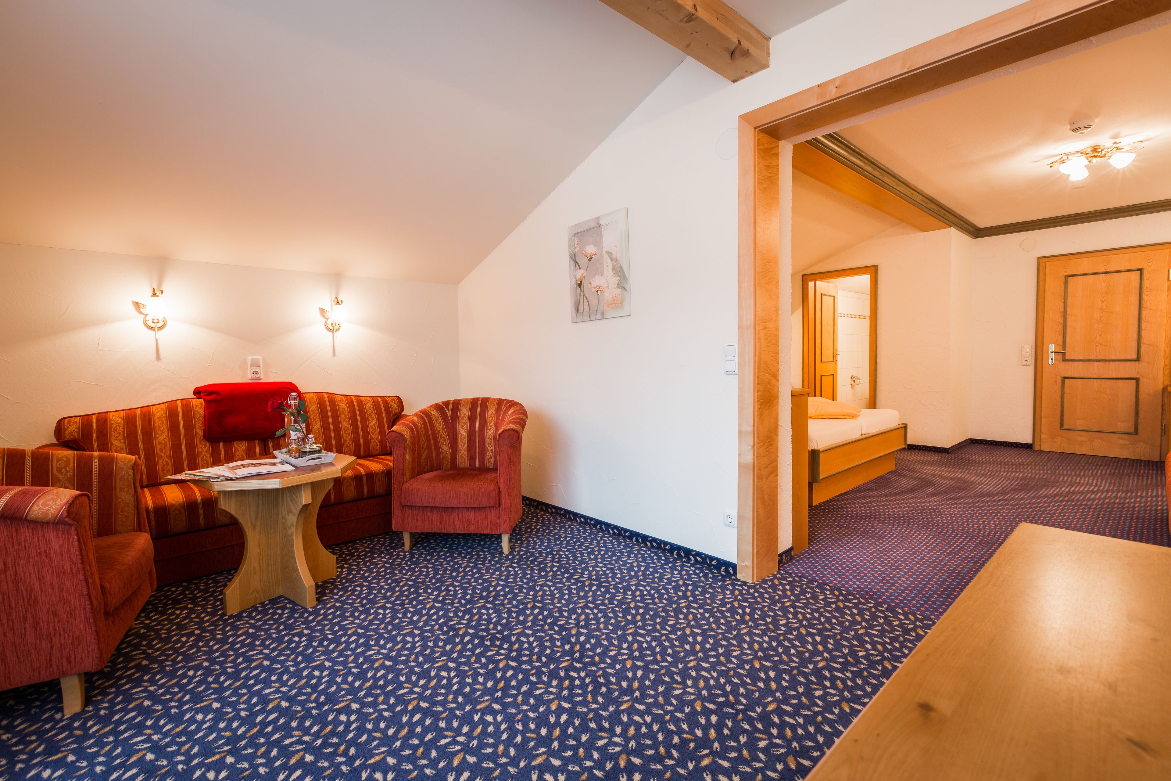 Una habitación acogedora con un sofá, sillones, una mesita y una puerta de madera que da a otra habitación.