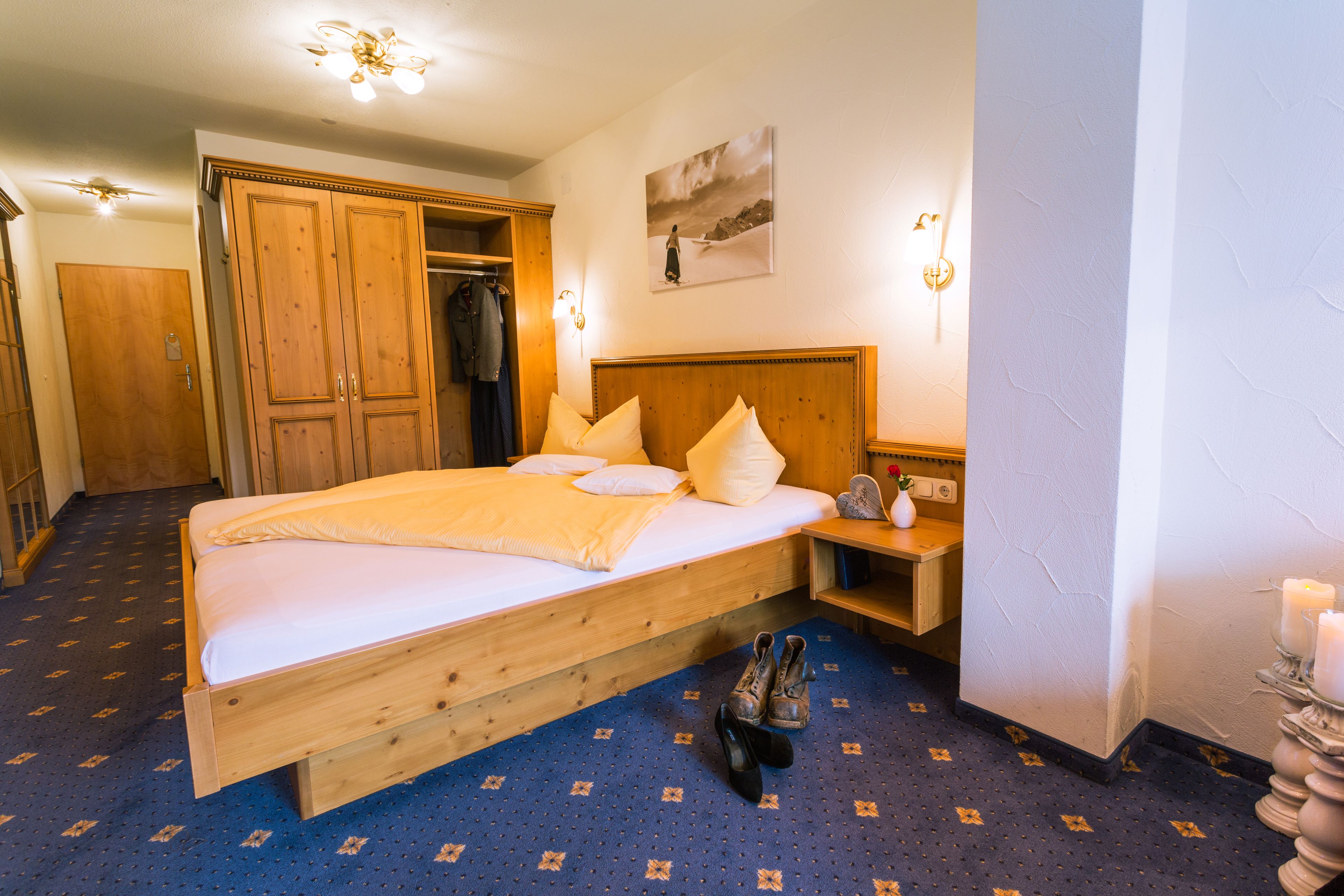 Un dormitorio con una cama de madera, un armario, un perchero y una mesita de noche con una vela.