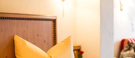 A bed with yellow bedding and pillows, a wooden headboard, and wall-mounted light fixtures.