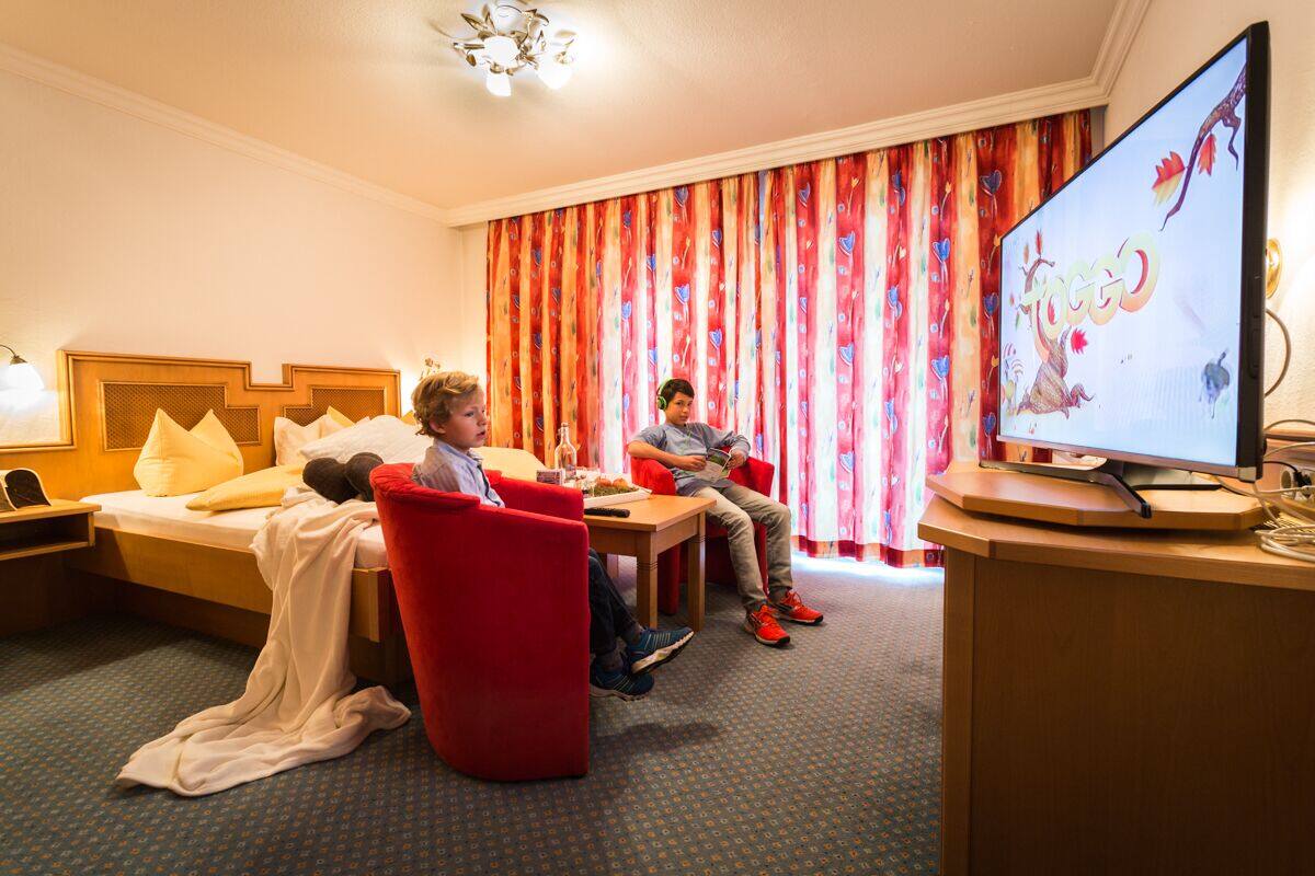Quarto de hotel com cama, escrivaninha, televisão e uma cadeira vermelha.