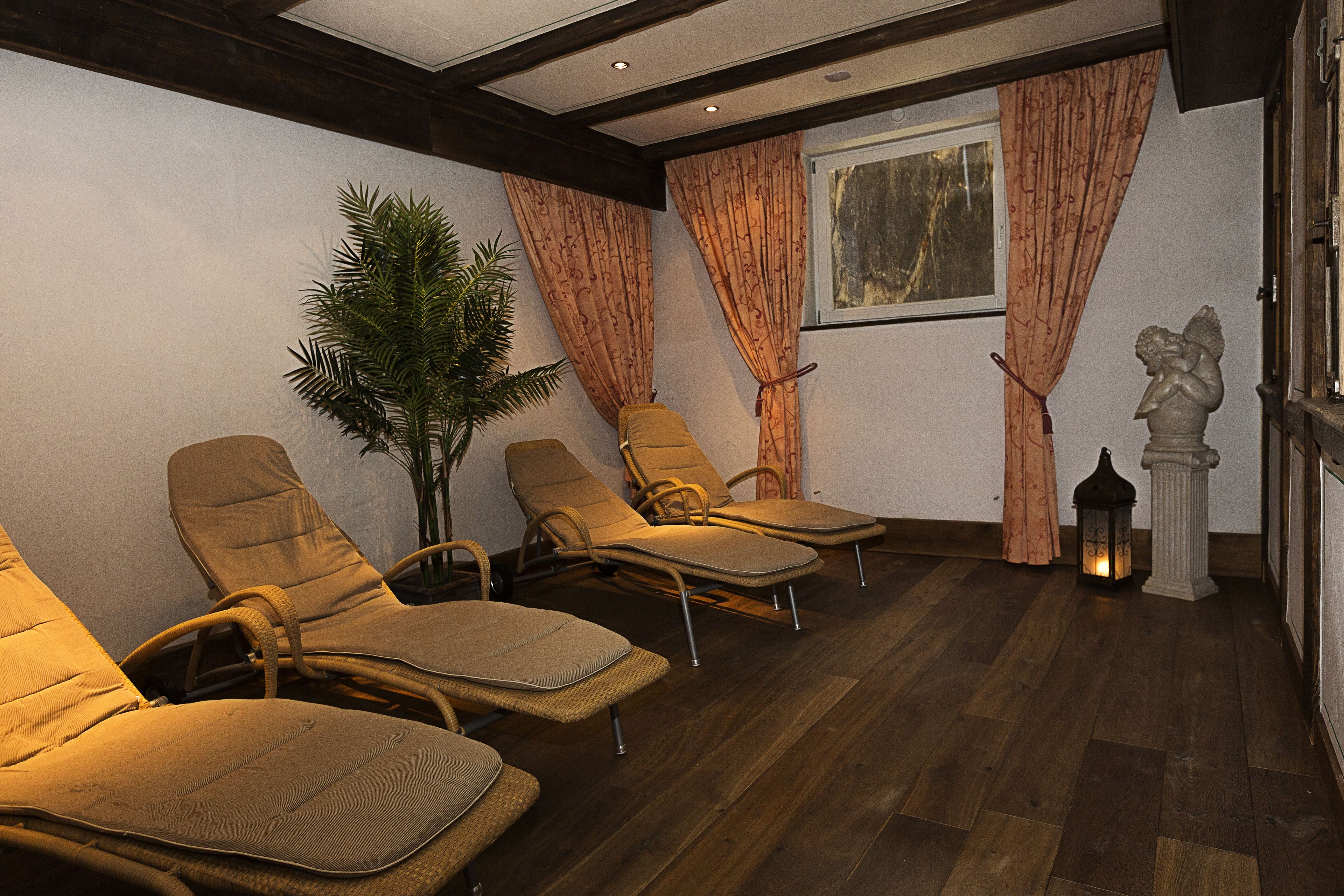 A room with four lounge chairs, a potted plant, a statue, and a window with curtains.