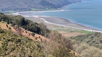 A coastal landscape with a beach, rolling hills, and a distant view of the sea.
