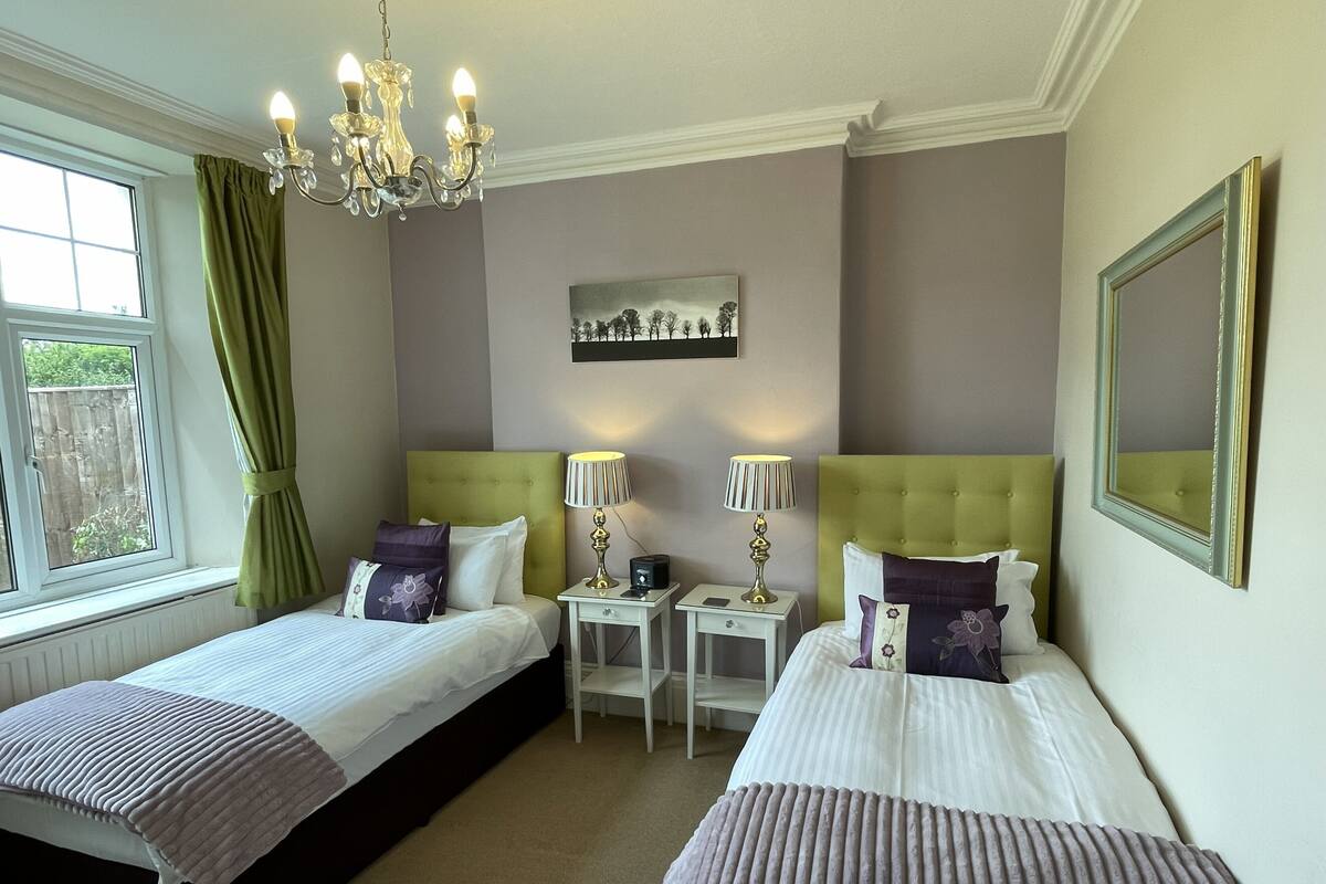 A hotel room with two beds, a chandelier, a painting, and a mirror.