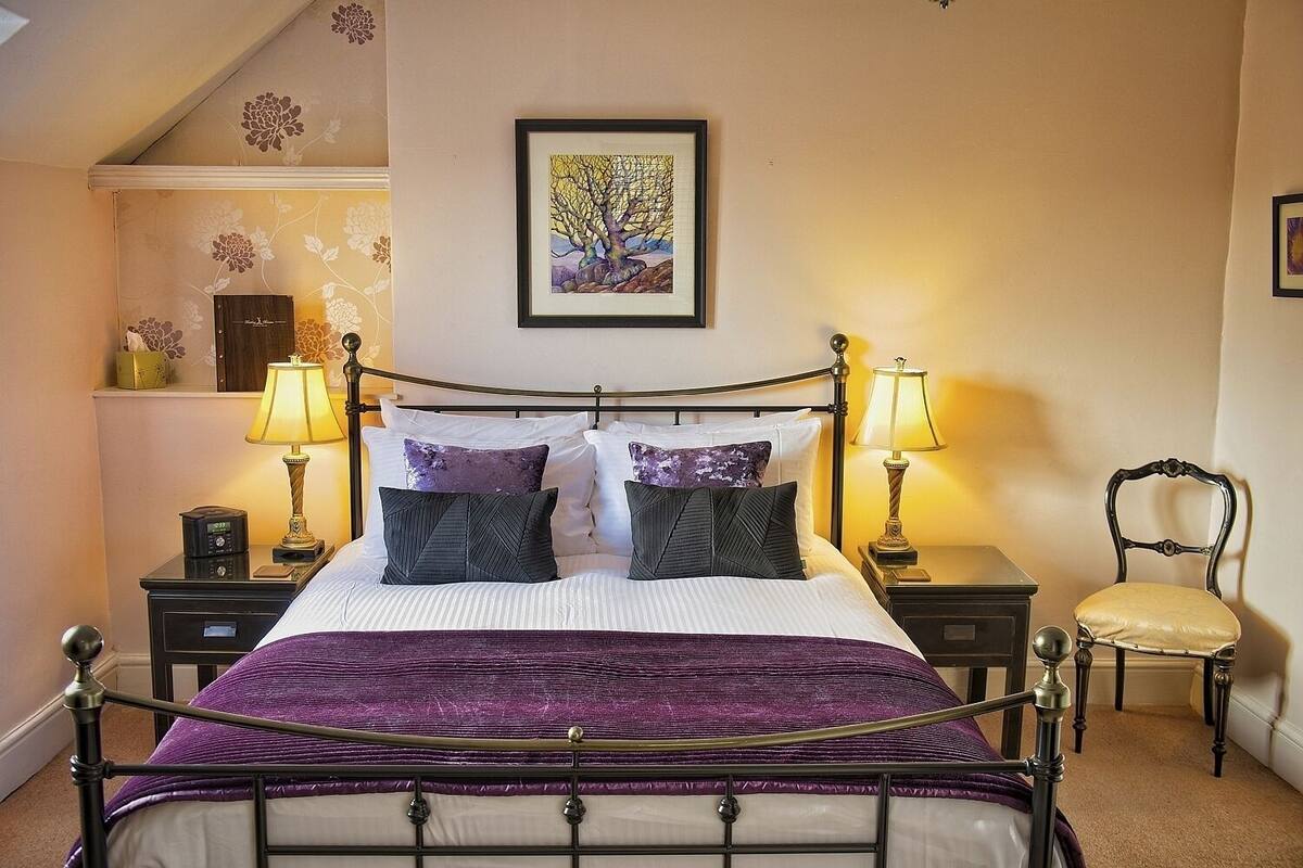 A neatly arranged bedroom with a bed, two bedside tables, a chair, and a framed artwork on the wall.