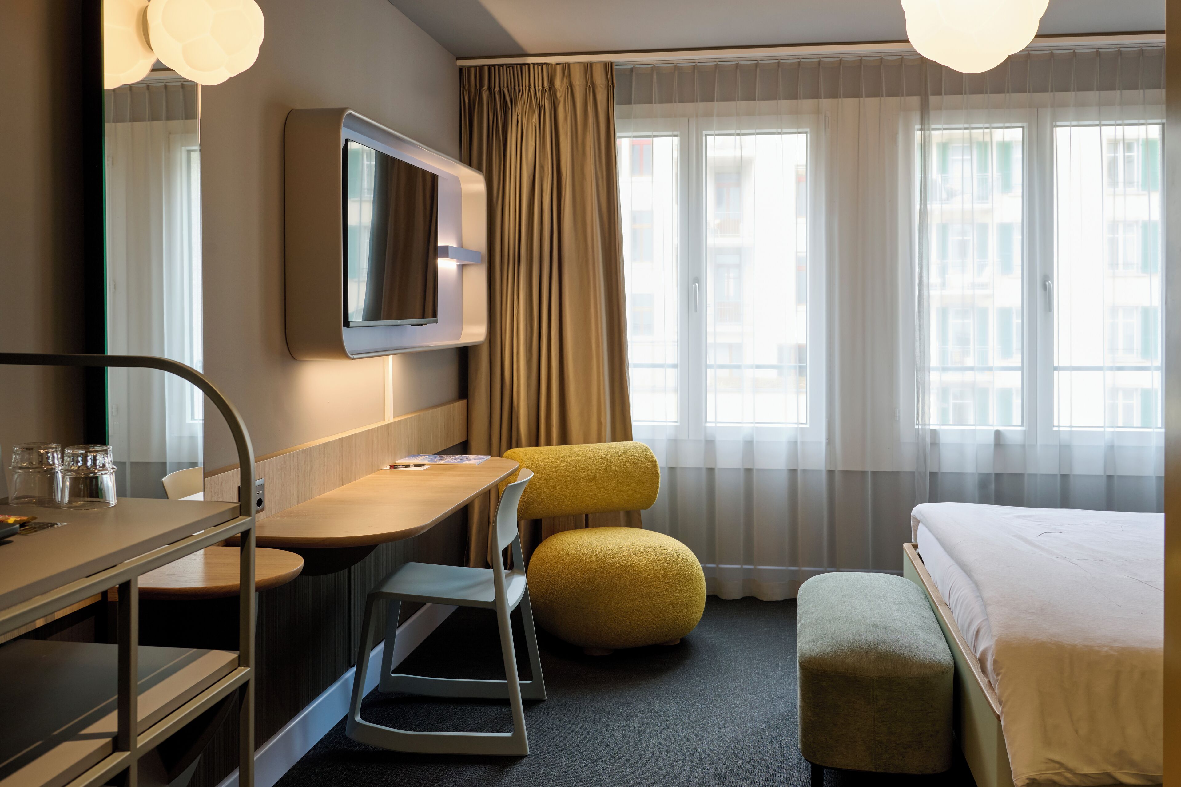 A hotel room with a bed, a desk with a chair, a television, and a window with curtains.