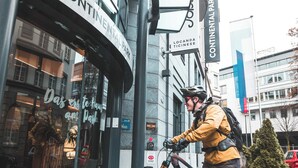 A person in a yellow jacket and helmet, wearing cycling gear, dismounting a bicycle in front of a building with a glass facade and signage reading "CONTINENTAL PARK". - Hotel Continental Park (Lucerne)