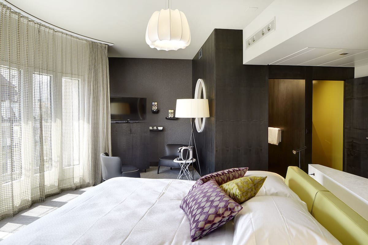 A modern hotel room with a large bed, a desk, a chair, and a television.