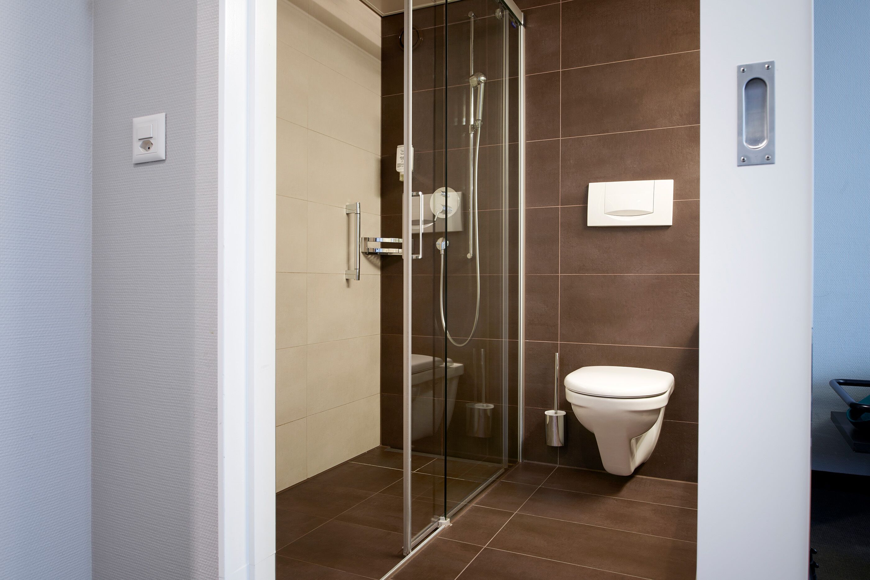 A modern bathroom with a glass-enclosed shower, a white toilet, and a towel dispenser.