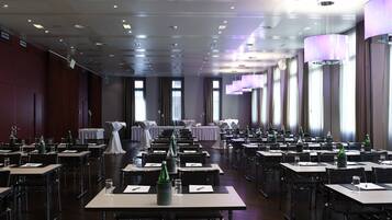 Una sala conferenze con file di tavoli, sedie e un palco con una tovaglia bianca.