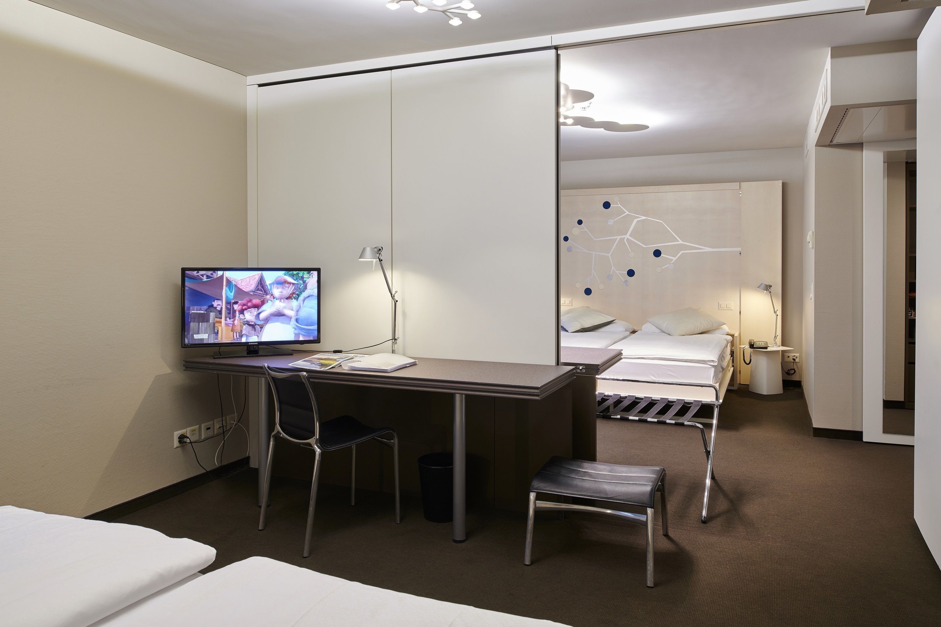 A hotel room with a desk, chair, bed, and a TV on the desk.