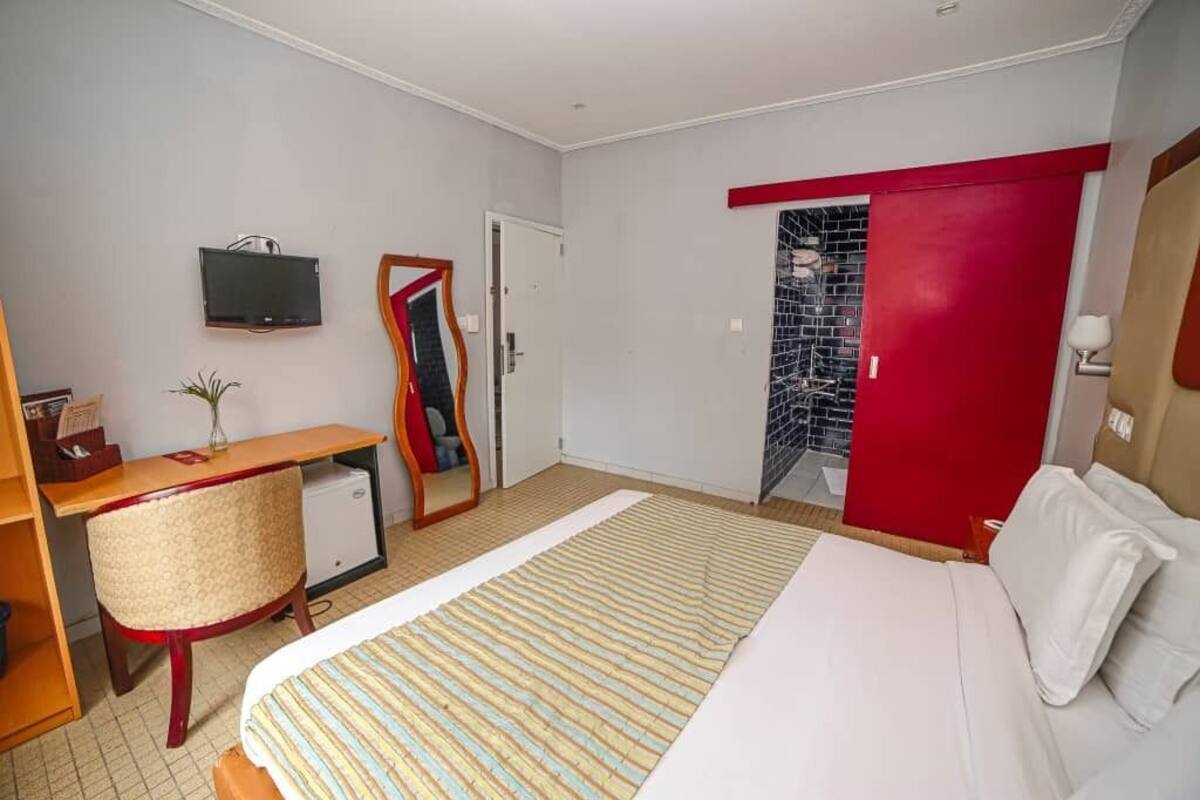 Habitación de hotel con cama, escritorio, silla, televisor y una puerta roja.
