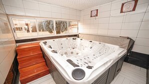 A modern bathroom with a large bathtub, wooden steps, and a view through a window. - Fini Hotel Bobende (Limbe)