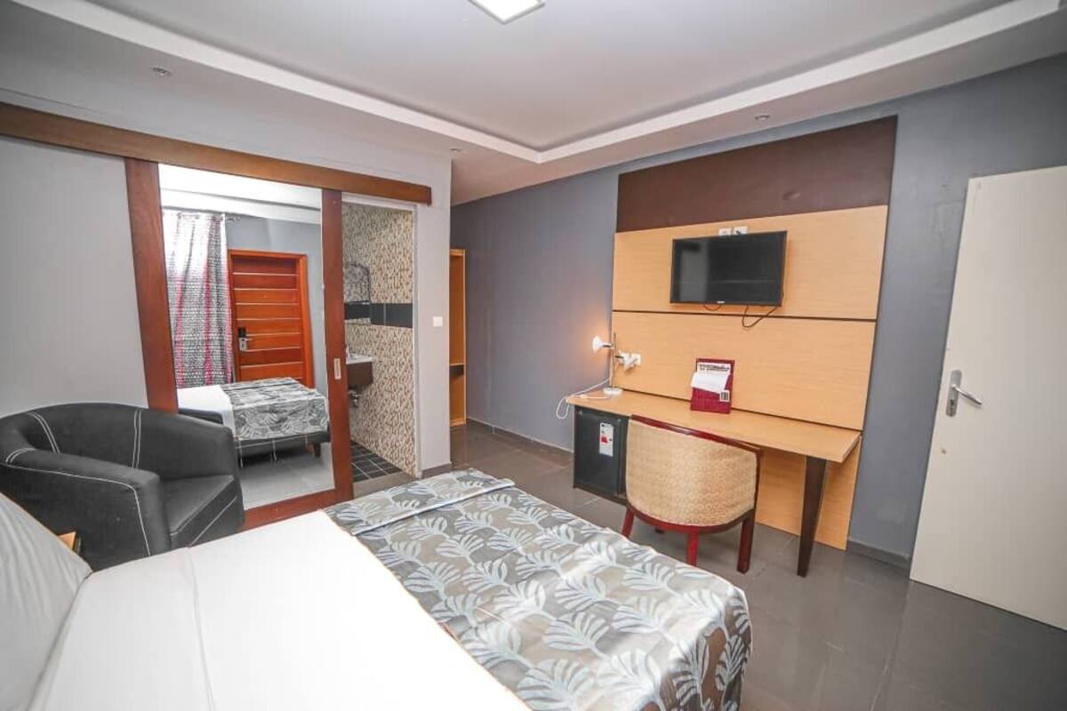 Una habitación de hotel con cama, escritorio, silla, televisor y armario.