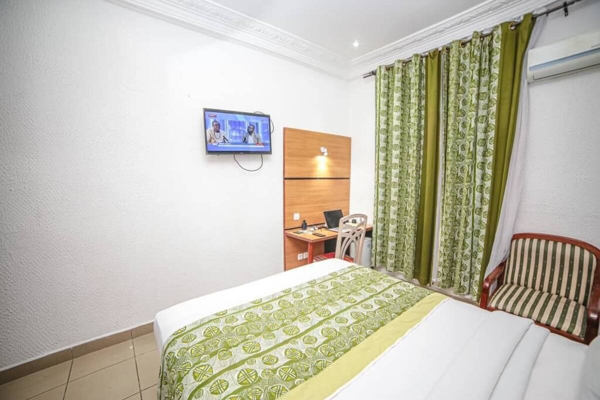 Una habitación de hotel con cama, escritorio y silla, televisor en la pared y cortinas.