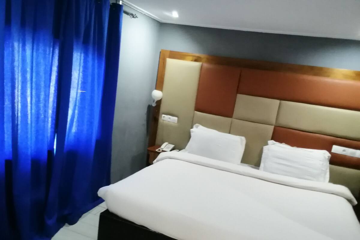 Una habitación de hotel con cama, mesita de noche, teléfono y lámpara de pared.