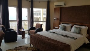 A hotel room with a large bed, a chair, a small table, and a view of the outside. - Fini Hotel Bobende (Limbe)