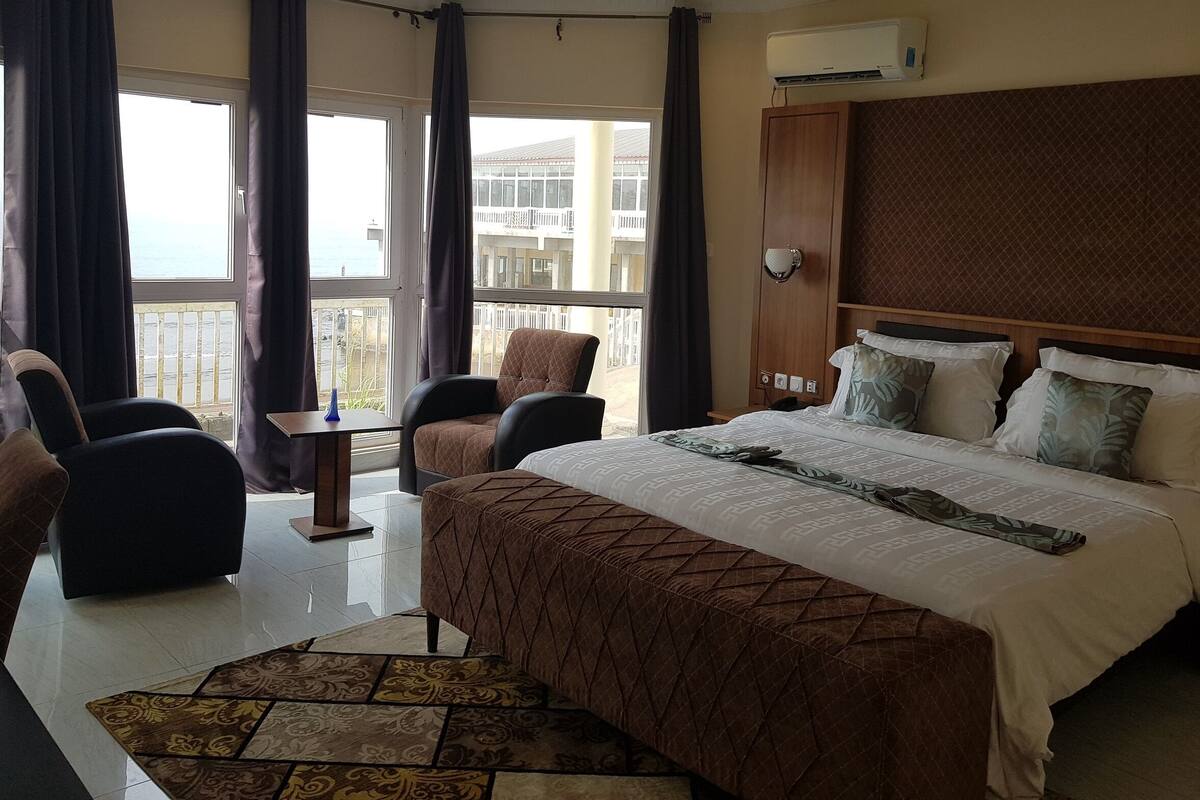 Habitación de hotel con una cama grande, una silla, una mesita y vistas al exterior.
