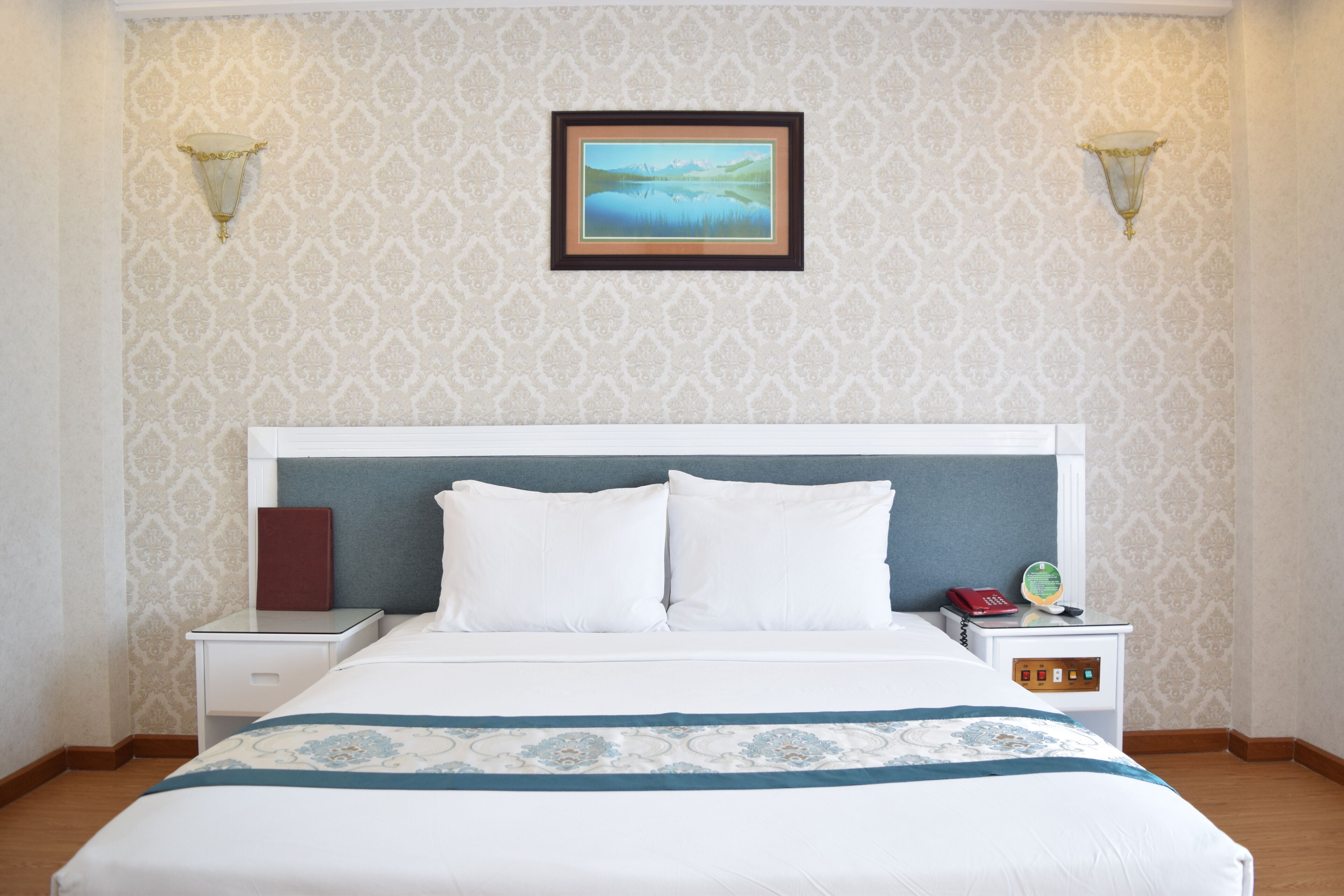 A hotel room with a bed, nightstands, a framed picture, and wall sconces.