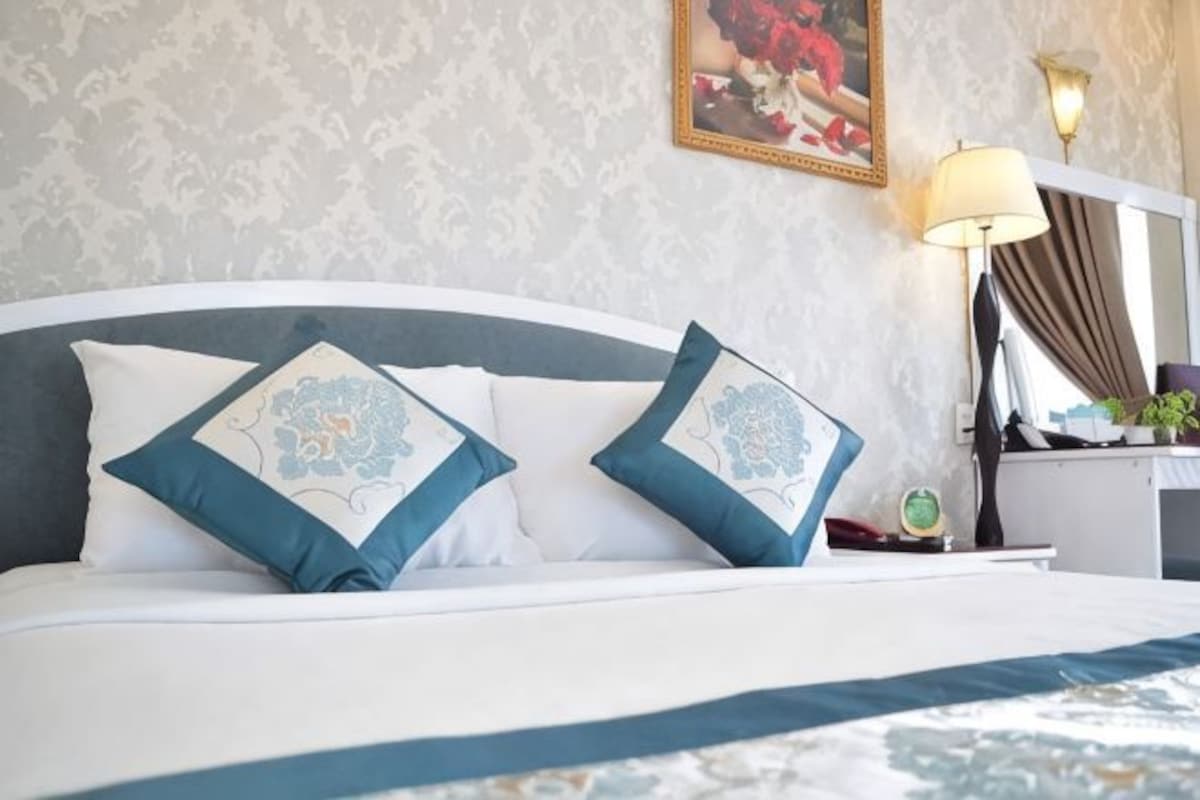 A bed with two decorative pillows, a bedside table with a lamp, and a framed picture on the wall.