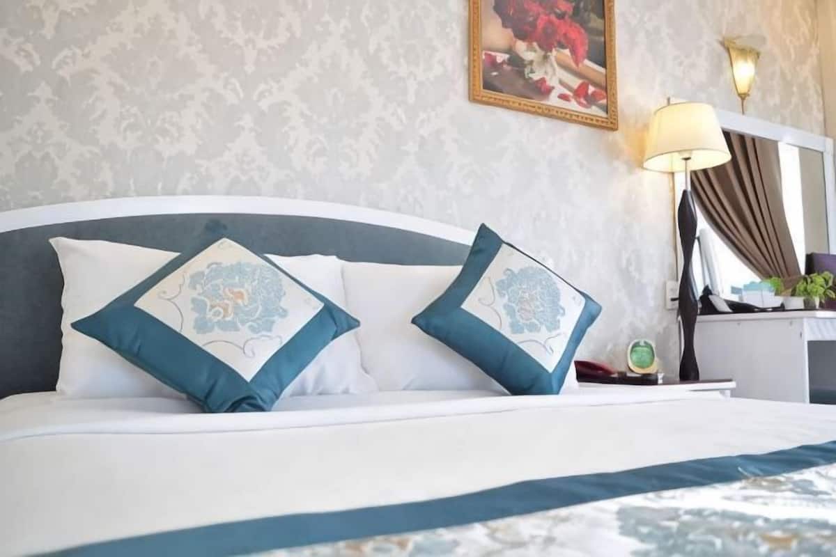 Uma cama com duas almofadas decorativas, uma mesa de cabeceira com abajur e um quadro na parede.