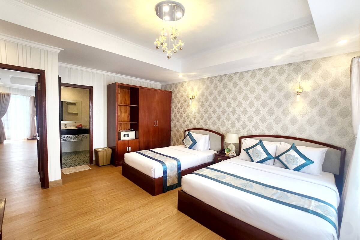 Quarto de hotel com duas camas, um guarda-roupa, uma penteadeira com espelho e um candelabro.