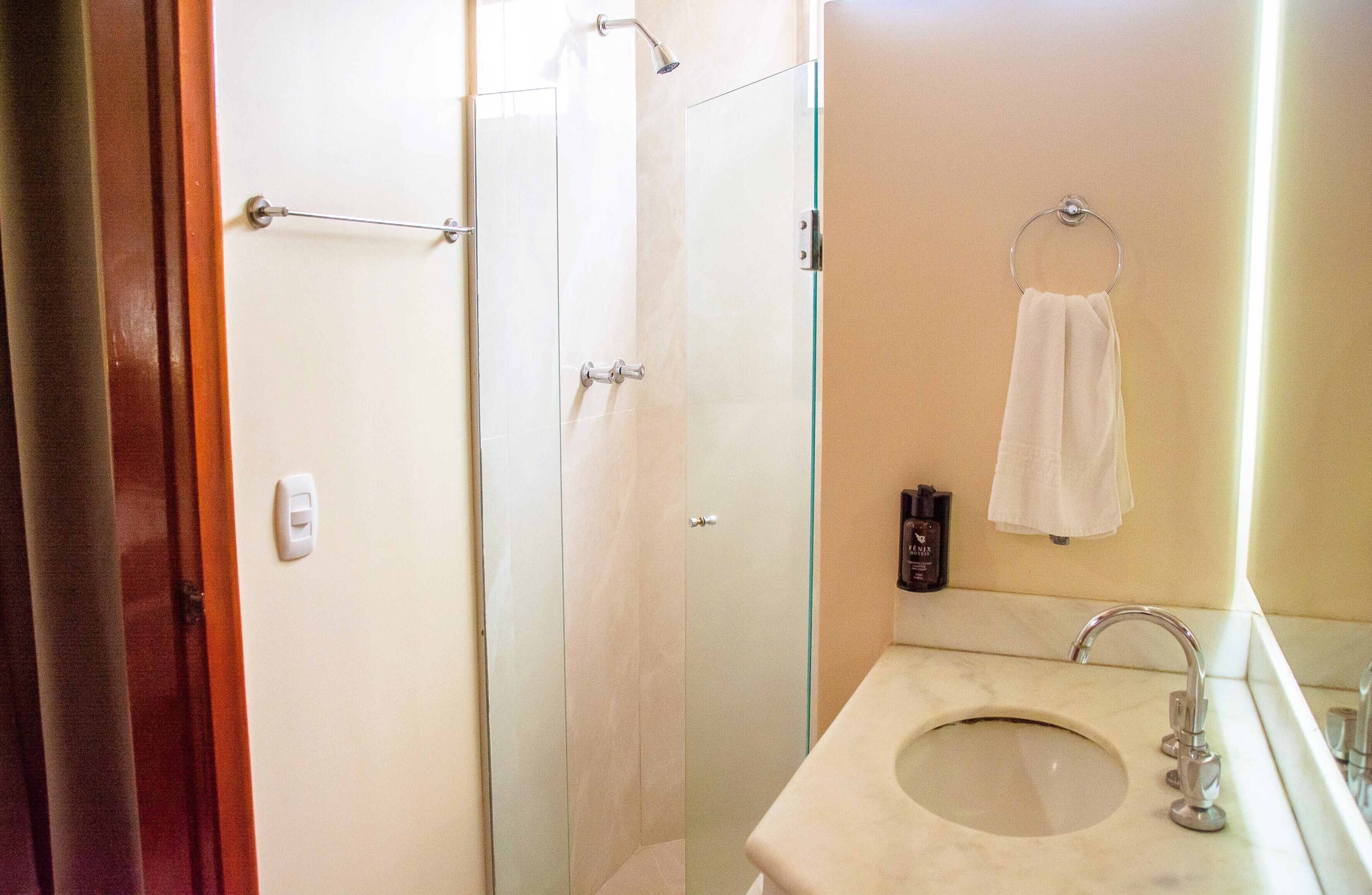 A bathroom with a glass shower enclosure, a sink with a mirror, and a towel hanging on a hook.