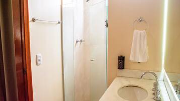 A bathroom with a glass shower enclosure, a sink with a mirror, and a towel hanging on a hook.